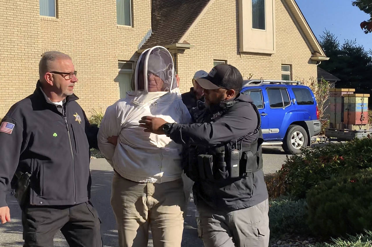 Rorie S. Woods, 55, of Hadley, Mass., center, wears a beekeeping suit while taken into custody by H...