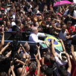 
              El expresidente Luiz Inácio Lula da Silva, al centro, sostiene una bandera de Brasil rodeado por simpatizantes tras depositar su voto en la segunda ronda electoral, el domingo 30 de octubre de 2022, en Sao Paulo, Brasil. (AP Foto/André Penner)
            