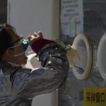 
              A woman pulls her face mask to get her routine COVID-19 throat swab at a coronavirus testing site in Beijing, Thursday, Oct. 6, 2022. Sprawling Xinjiang is the latest Chinese region to be hit with sweeping COVID-19 travel restrictions, as China further ratchets up control measures ahead of a key Communist Party congress later this month. (AP Photo/Andy Wong)
            