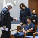 
              Yoni Barrios listens to Scott Coffee, left, and Jeff Maningo, public defenders, during a status check on the filing of a criminal complaint at the Regional Justice Center, on Tuesday, Oct. 11, 2022, in Las Vegas. Barrios is a suspect in a stabbing rampage on the Las Vegas Strip that left two people dead and six injured. (Bizuayehu Tesfaye /Las Vegas Review-Journal via AP)
            