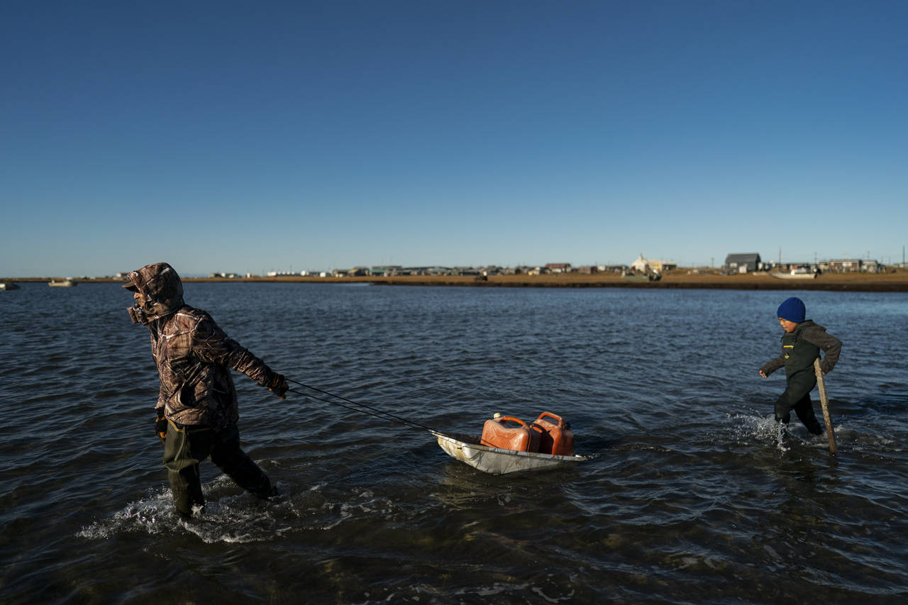 Pulling a sled with fuel containers in the lagoon, Joe Eningowuk, 62, left, and his 7-year-old gran...