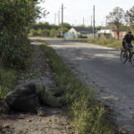 
              EDS NOTE: GRAPHIC CONTENT - A local man rides his bicycle past the dead body of a Russian serviceman in the recently liberated town of Kupiansk, Ukraine, Saturday, Oct. 1, 2022. (AP Photo/Evgeniy Maloletka)
            