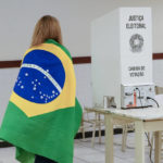 
              A voter wrapped in a Brazilian flag arrives to vote in a presidential a run-off pitting President Jair Bolsonaro against former President Luiz Inácio Lula da Silva, in Brasilia, Brazil, Sunday, Oct. 30, 2022. (AP Photo/Eraldo Peres)
            