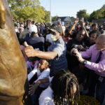 
              Audience members reach forward to touch and photograph the Emmett Till Memorial Statue following its unveiling, Friday, Oct. 21, 2022, in Greenwood, Miss. White men kidnapped and killed 14-year-old Till in August 1955 over accusations that he flirted with a white woman in a county store. His lynching became a catalyst for the civil rights movement after his mother Mamie Till Mobley, insisted on a open-casket funeral for her son in Chicago, where they lived. Till had traveled to Mississippi that summer to visit relatives. (AP Photo/Rogelio V. Solis)
            