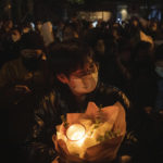 
              A protester holds flower and candles in Beijing, Sunday, Nov. 27, 2022. Protesters angered by strict anti-virus measures called for China's powerful leader to resign, an unprecedented rebuke as authorities in at least eight cities struggled to suppress demonstrations Sunday that represent a rare direct challenge to the ruling Communist Party. (AP Photo/Ng Han Guan)
            