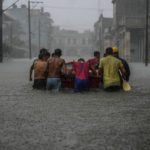 
              FILE - Residents push a boat through a flooded street to rescue a neighbor unable to leave his home on his own during a tropical cyclone in Havana, Cuba, June 3, 2022. Loss and damage is the human side of a contentious issue that will likely dominate climate negotiations in Egypt. (AP Photo/Ramon Espinosa, File)
            