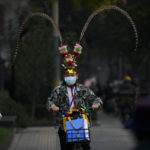 
              A man wearing a face mask dressed with Monkey King costume headgear rides past masked residents on a street in Beijing, Wednesday, Nov. 2, 2022. (AP Photo/Andy Wong)
            