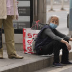 
              FILE - An elderly woman wearing mask waits at a bus-stop in Chaoyang District on Monday, April 25, 2022, in Beijing. (AP Photo/Ng Han Guan, File)
            