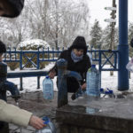 
              People collect water, in Kyiv, Ukraine, Thursday, Nov. 24, 2022. Residents of Ukraine's bombed but undaunted capital clutched empty bottles in search of water and crowded into cafés for power and warmth Thursday, switching defiantly into survival mode after new Russian missile strikes a day earlier plunged the city and much of the country into the dark. 
 (AP Photo/Evgeniy Maloletka)
            