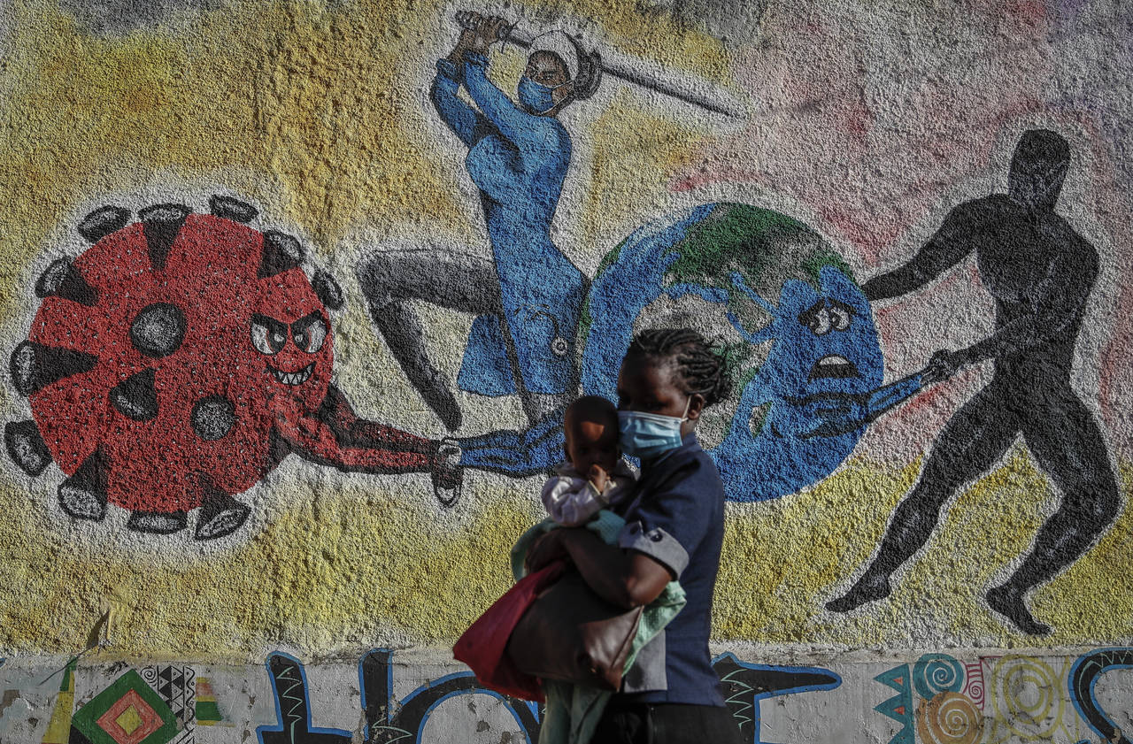 FILE - A woman and child walk past an informational mural portraying the global battle against the ...