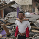 
              A man carries his son past ruins of houses damaged in Monday's earthquake in Cianjur, West Java, Indonesia Tuesday, Nov. 22, 2022. The earthquake has toppled buildings on Indonesia's densely populated main island, killing a number of people and injuring hundreds. (AP Photo/Tatan Syuflana)
            