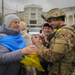 
              Kherson residents react as a Ukrainian soldier writes his wishes for a man wrapped in the national flag in central Kherson, Ukraine, Sunday, Nov. 13, 2022. The Russian retreat from Kherson marked a triumphant milestone in Ukraine's pushback against Moscow's invasion almost nine months ago.(AP Photo/Efrem Lukatsky)
            