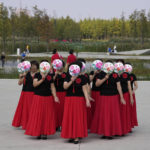 
              Residents hold up fans with flower designs to hide their faces as they dance at the "Fish Tail" sponge park that's built on a former coal ash dump site in Nanchang in north-central China's Jiangxi province on Sunday, Oct. 30, 2022. The concept of the park involves creating and expanding parks and ponds within urban areas to prevent flooding and absorb water for times of drought. (AP Photo/Ng Han Guan)
            