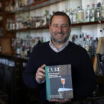 
              Neal Bodenheimer, owner and founder of Cure, poses in his craft cocktail bar with a copy of his new book "Cure: New Orleans Drinks and How to Mix 'Em" in New Orleans, Friday, Nov. 18, 2022. (AP Photo/Gerald Herbert)
            