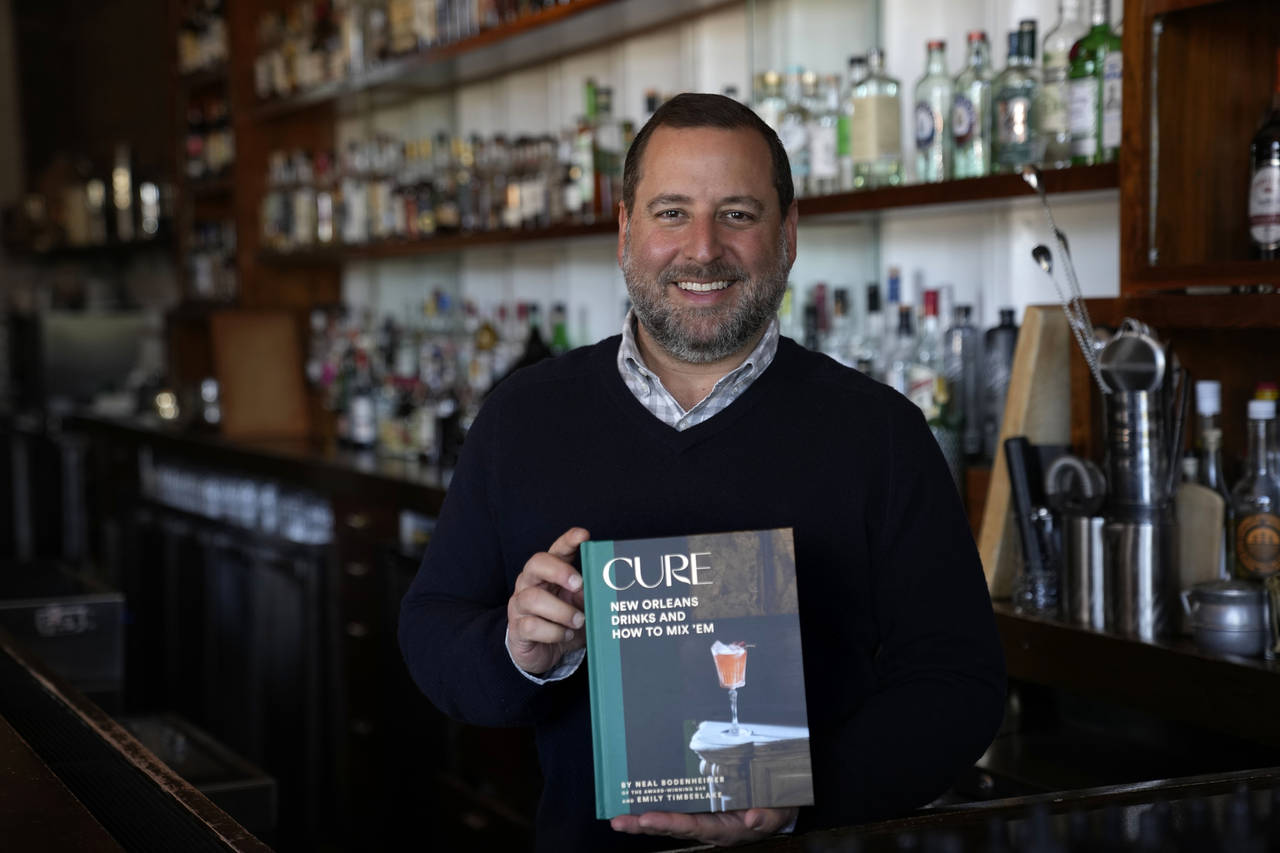 Neal Bodenheimer, owner and founder of Cure, poses in his craft cocktail bar with a copy of his new...