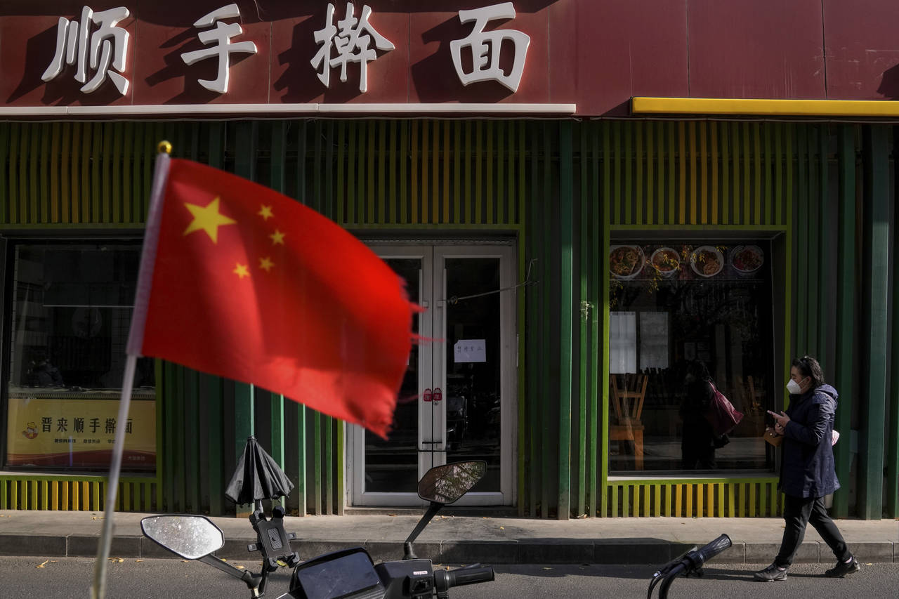 FILE - A woman wearing a face mask walks past a national flag outside a closed noodles restaurant d...