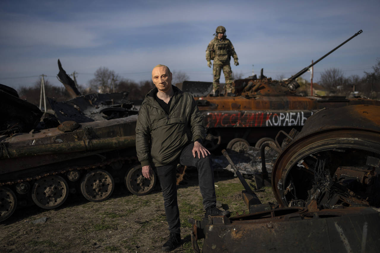 A civilian wears a Vladimir Putin mask as a spoof, while a Ukrainian soldier stands atop a destroye...