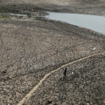 
              FILE - A man walks across a dried patch of the river Yamuna as water level reduces drastically following heat wave to in New Delhi, May 2, 2022. Loss and damage is the human side of a contentious issue that will likely dominate climate negotiations in Egypt. In India, it's record heat connected to climate change that caused deaths and ruined crops. (AP Photo/Manish Swarup, File)
            