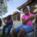 
              Nine-year-old Amalia Valdez, right, helps her grandmother Norma, center, peel corn at Naranjo's home in Ohkay Owingeh, formerly named San Juan Pueblo, in northern New Mexico, Sunday, Aug. 21, 2022. Friends and relatives of the Naranjos gather every year to make chicos, dried kernels used in stews and puddings. (AP Photo/Andres Leighton)
            