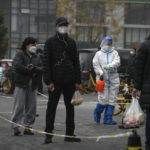 
              A worker in protective suit sprays disinfectant as residents stand in line for their routine COVID-19 throat swabs at a coronavirus testing site in Beijing, Thursday, Nov. 24, 2022. China is expanding lockdowns, including in a central city where factory workers clashed this week with police, as its number of COVID-19 cases hit a daily record. (AP Photo/Andy Wong)
            