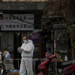 
              A worker in protective gear sanitizes his gloves outside a locked down neighborhood as part of COVID-19 controls in Beijing, Monday, Nov. 28, 2022. Authorities eased anti-virus rules in scattered areas but affirmed China's severe "zero- COVID" strategy Monday after crowds demanded President Xi Jinping resign during protests against controls that confine millions of people to their homes. (AP Photo/Andy Wong)
            