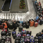 
              Airport staff and a person walks around a pile of lost suitcases near the baggage carousel at Midway Airport in Chicago, Tuesday, Dec. 27, 2022, after Southwest Airlines flights were cancelled and delayed during a winter storm.  Problems at Southwest Airlines appeared to snowball after the worst of the storm passed. It cancelled more than 70% of its flights Monday, more than 60% on Tuesday, and warned that it would operate just over a third of its usual schedule in the days ahead to allow crews to get back to where they needed to be. (Pat Nabong /Chicago Sun-Times via AP)
            
