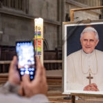
              A person takes a picture of a portrait of Pope Emeritus Benedict XVI at St. Peter's Cathedral in Regensburg, Germany, Saturday, Dec. 31, 2022. Pope Emeritus Benedict XVI, the German theologian who will be remembered as the first pope in 600 years to resign, has died, the Vatican announced Saturday. He was 95. (Armin Weigl/dpa via AP)
            