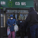 
              A woman carries a bag of cold and fever medicine as residents line up for medicine at a pharmacy in Beijing, Sunday, Dec. 11, 2022. Facing a surge in COVID-19 cases, China is setting up more intensive care facilities and trying to strengthen hospitals as Beijing rolls back anti-virus controls that confined millions of people to their homes, crushed economic growth and set off protests. (AP Photo/Andy Wong)
            