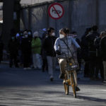 
              A masked woman bicycles past residents lining up to enter the fever clinic of a hospital in Beijing, Sunday, Dec. 11, 2022. Facing a surge in COVID-19 cases, China is setting up more intensive care facilities and trying to strengthen hospitals as Beijing rolls back anti-virus controls that confined millions of people to their homes, crushed economic growth and set off protests. (AP Photo/Andy Wong)
            