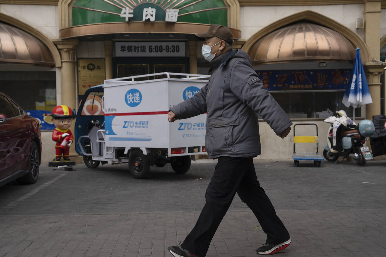 A man wearing a mask walks near a restaurant in Beijing, Friday, Dec. 2, 2022. More cities eased re...