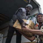 
              FILE - Timothy Boarman, left, and Swanson Owens unload a truck of fresh produce to be given out to people affected by the Tops Friendly Market closure on May 17, 2022, in Buffalo, N.Y. After mass shootings, the loss felt by marginalized groups already facing discrimination is compounded. Some public health experts say the risk for post-traumatic stress disorder is greater for the groups, especially when the shootings take place at schools, churches and other vital hubs. (AP Photo/Joshua Bessex)
            