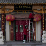 
              A masked worker on a ladder cleans a dusty lantern outside a steamboat restaurant at the Wangfujing shopping district in Beijing, Wednesday, Dec. 14, 2022. China's National Health Commission scaled down its daily COVID-19 report starting Wednesday in response to a sharp decline in PCR testing since the government eased anti-virus measures and daily cases hit record highs. (AP Photo/Andy Wong)
            
