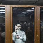 
              Russian opposition activist and former municipal deputy of the Krasnoselsky district Ilya Yashin gestures as he stands inside a glass cubicle in a courtroom prior to a hearing in Moscow, Russia, Friday, Dec. 9, 2022.  Yashin has been sentenced to 8 1/2 years in prison on charges stemming from his criticism of the Kremlin's action in Ukraine. The sentence handed Friday to Yashin, one of the few Kremlin critics to have remained in the country, marked the latest move in an intensifying crackdown on dissent. (Yury Kochetkov/Pool Photo via AP)
            