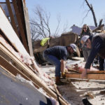 
              Belinda Penner, center, watches as Jr. Ibarra, left, and Jared Reaves, right, carry a beam from her cousin's tornado destroyed home, Tuesday, Dec. 13, 2022, in Wayne, Okla. (AP Photo/Sue Ogrocki)
            