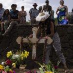
              A person places a karone tiare necklace of flowers on the gravesite cross of local horse breeder and former military diver Emilio Araki during his burial at the cemetery in Hanga Roa, Rapa Nui, or Easter Island, Chile, Saturday, Nov. 26, 2022. The first Europeans arrived to Rapa Nui in 1722, soon followed by missionaries, when Rapanui religiosity began to intertwine with Christianity. (AP Photo/Esteban Felix)
            