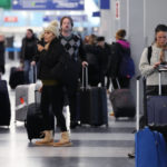 
              A traveler, right, checks on her cellphone as other travelers walk through Terminal 3 at O'Hare International Airport in Chicago, Thursday, Dec. 22, 2022. (AP Photo/Nam Y. Huh)
            