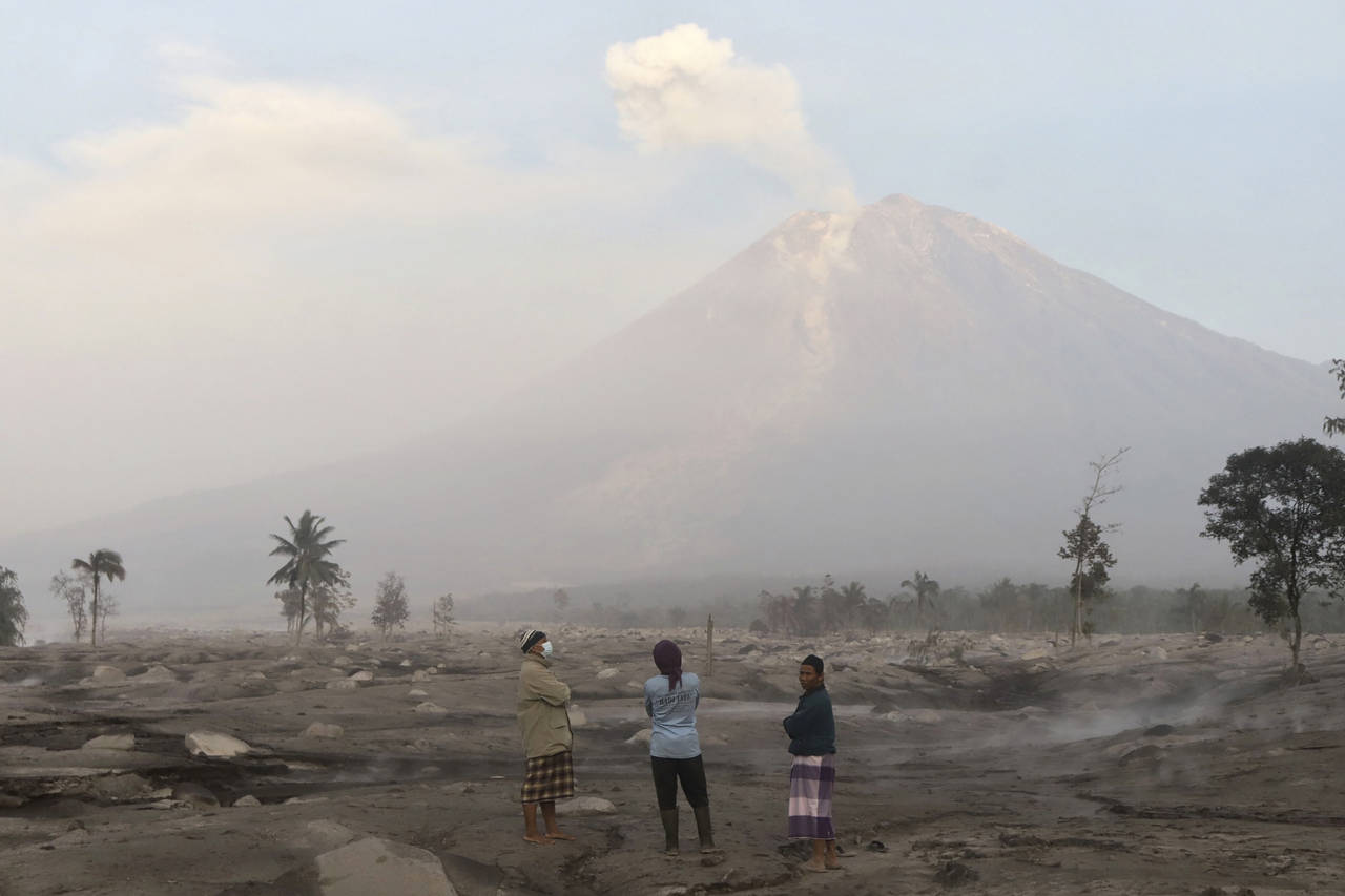 Villagers stand on an area covered in volcanic ash as Mount Semeru looms in the background in Kajar...