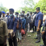 
              Security officers stand by Rohingya refugees after they arrived on Indra Patra beach in Ladong village, Aceh province, Indonesia, Sunday, Dec. 25, 2022. Dozens of hungry and weak Rohingya Muslims were found on a beach in Indonesia's northernmost province of Aceh on Sunday after weeks at sea, officials said. (AP Photo/Rahmat Mirza)
            