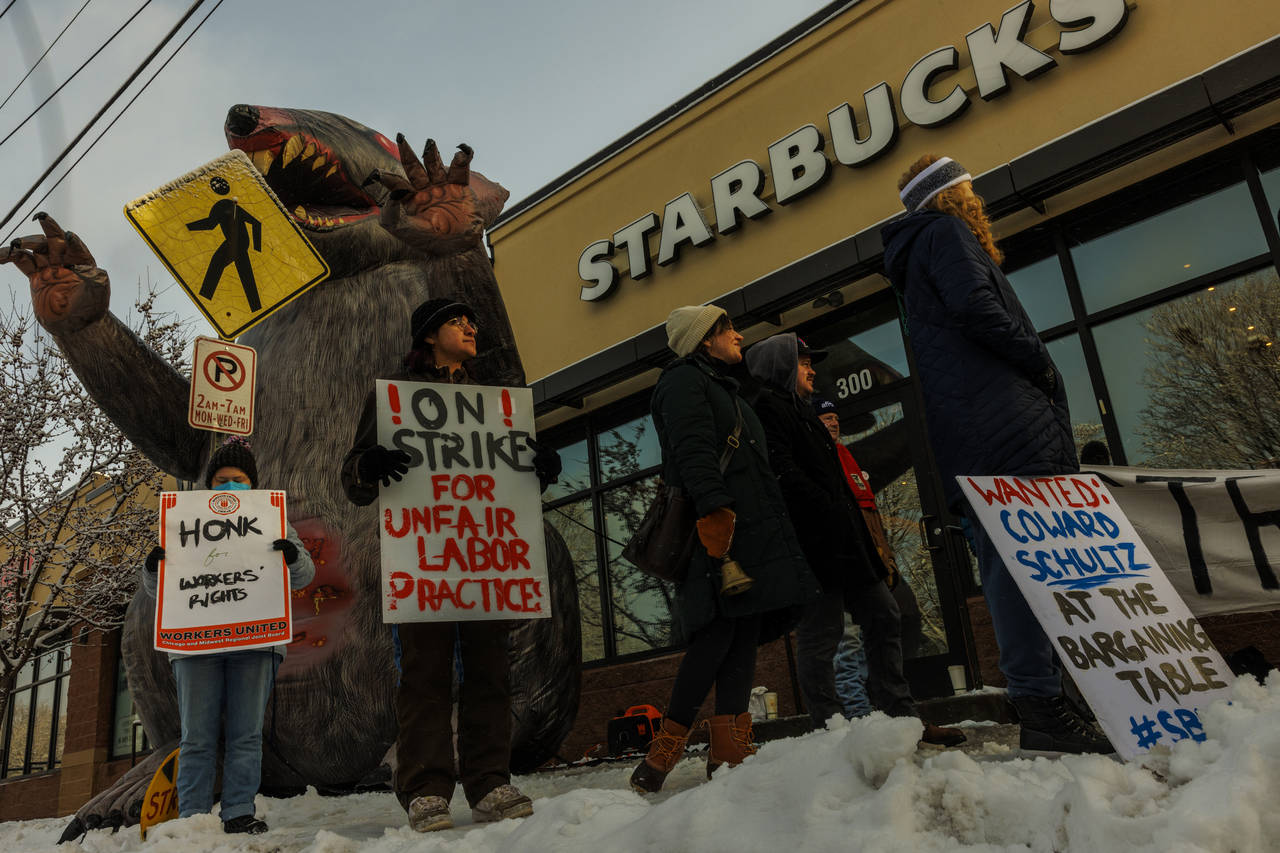 Starbucks workers hold signs in front of a giant inflatable rat during the "Unfair Labor Practice S...