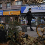 
              A man walks by a bicycle of bike-sharing company covered with tree leaves near reopened shops after authorities start easing some of the anti-virus controls in Beijing, Wednesday, Dec. 7, 2022. China has announced new measures rolling back COVID-19 restrictions, including limiting lockdowns and testing requirements. (AP Photo/Andy Wong)
            