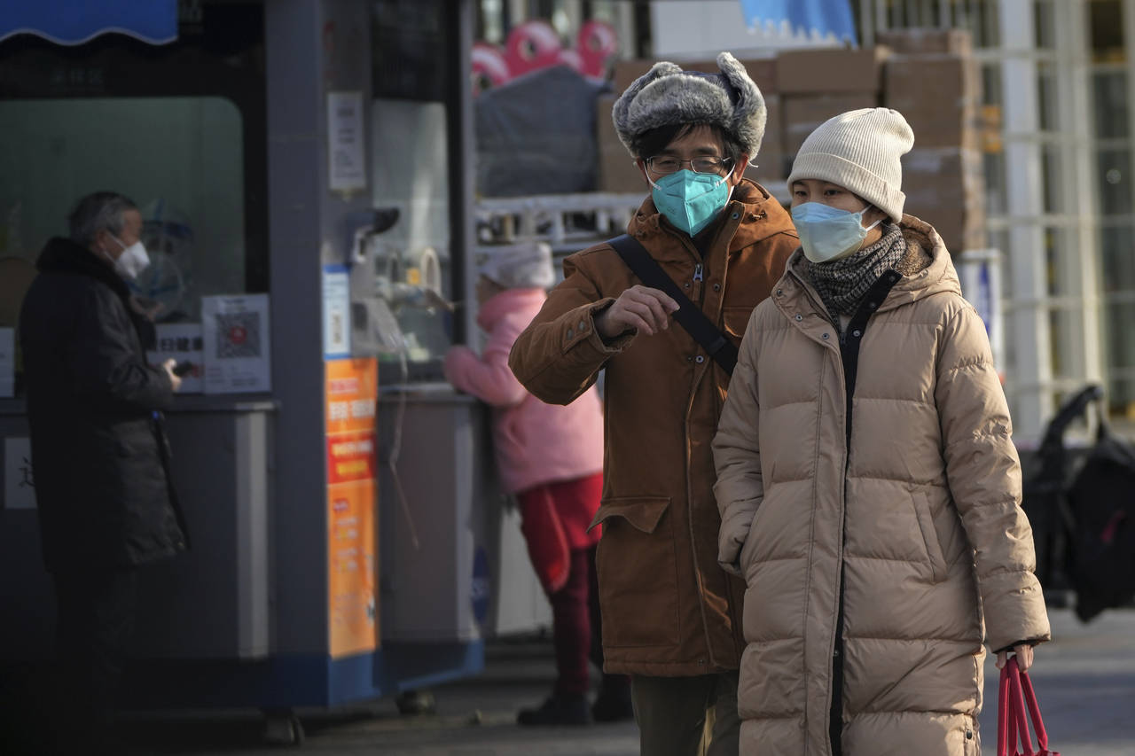 A couple wearing face masks walk past residents get their routine COVID-19 throat swabs at a corona...