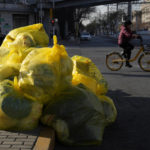 
              A cyclist passes by household waste inside yellow trash bags marked as medical waste in Beijing, Wednesday, Dec. 7, 2022. In a sharp reversal, China has announced a series of measures rolling back some of the most draconian anti-COVID-19 restrictions. (AP Photo/Ng Han Guan)
            