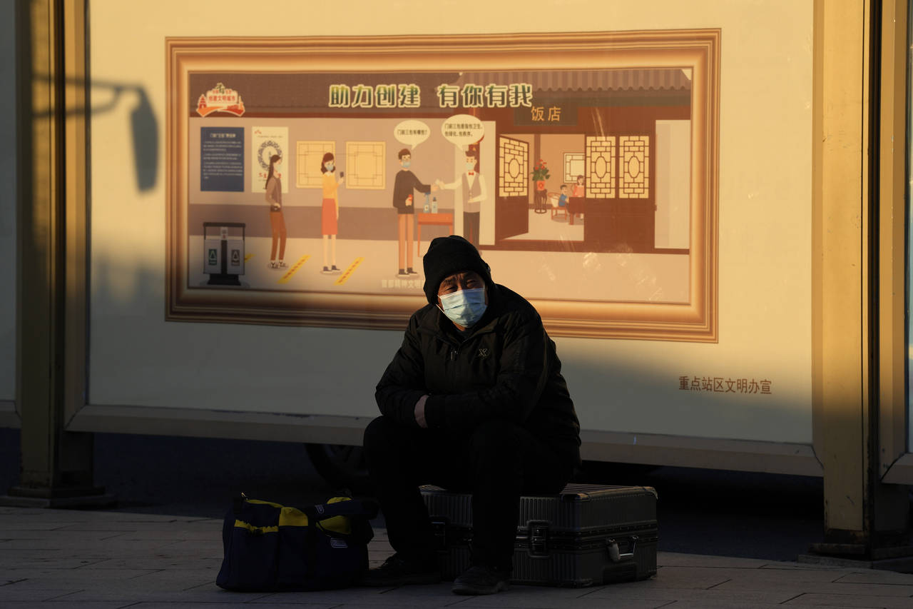 A man wearing a mask sits on his luggage near a mural depicting health checks before entry to a res...