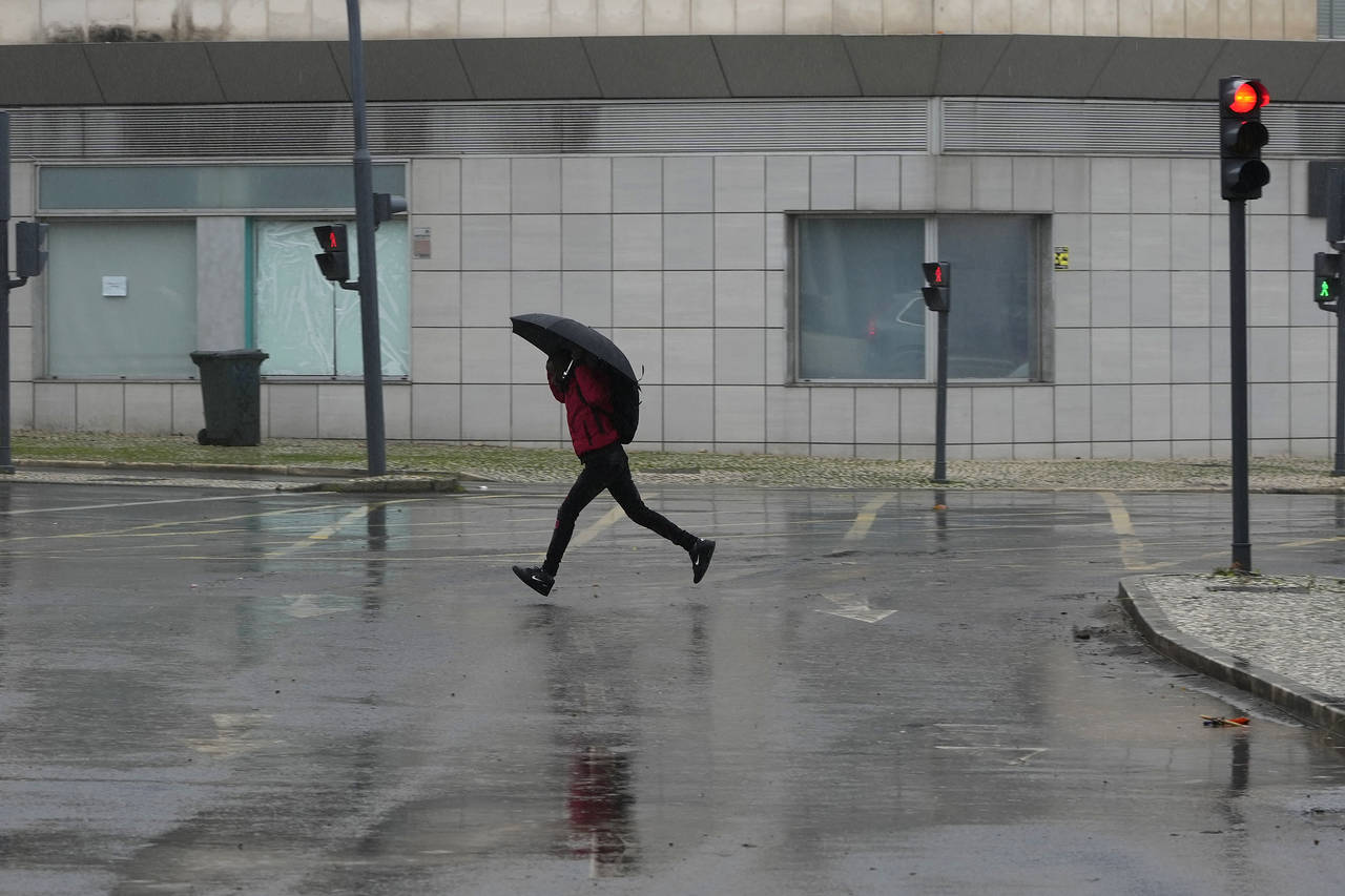 A man runs across a street under the rain in Alges, just outside Lisbon, Tuesday, Dec. 13, 2022. An...