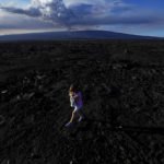 
              Abigail Dewar, of Alberta, Canada, holds a stuffed animal as she walks over hardened lava rock from a previous eruption as the Mauna Loa volcano erupts, behind, Wednesday, Nov. 30, 2022, near Hilo, Hawaii. (AP Photo/Gregory Bull)
            