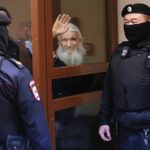 
              Nikolai Romanov, a former monk known as Father Sergiy until he was excommunicated by the Russian Orthodox Church, waves standing behind a glass cage during his trial in Moscow, Russia, Friday, Jan. 27, 2023. The monk, who denied that the coronavirus existed and challenged the Kremlin, was handed a new prison sentence Friday on charges of inciting hatred. (AP Photo/Alexander Zemlianichenko)
            