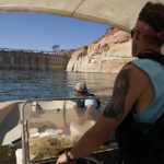
              FILE - Utah State University master's student Barrett Friesen steers a boat near Glen Canyon dam on Lake Powell on June 7, 2022, in Page, Ariz. Six western states that rely on water from the Colorado River have agreed on a plan to dramatically cut their use. California, the state with the largest allocation of water from the river, is the holdout. (AP Photo/Brittany Peterson, File)
            