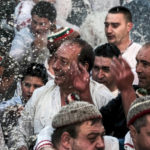 
              A man smiles, seen though splashes of water during men's dance into the cold Tundzha River, during Epiphany ritual in the town of Kalofer, Friday, Jan. 6, 2023. The legend goes that the person who retrieves the wooden cross will be freed from evil spirits and will be healthy throughout the year. After the cross is fished out, the priest delivers a special blessing to that man and his household. In the small mountain city of Kalofer in central Bulgaria the ritual lasts longer, as nearly a hundred men dressed in traditional white embroidered shirts wade into the Tundzha River to perform a slow men's dance. (AP Photo/Alexander Nikolov)
            