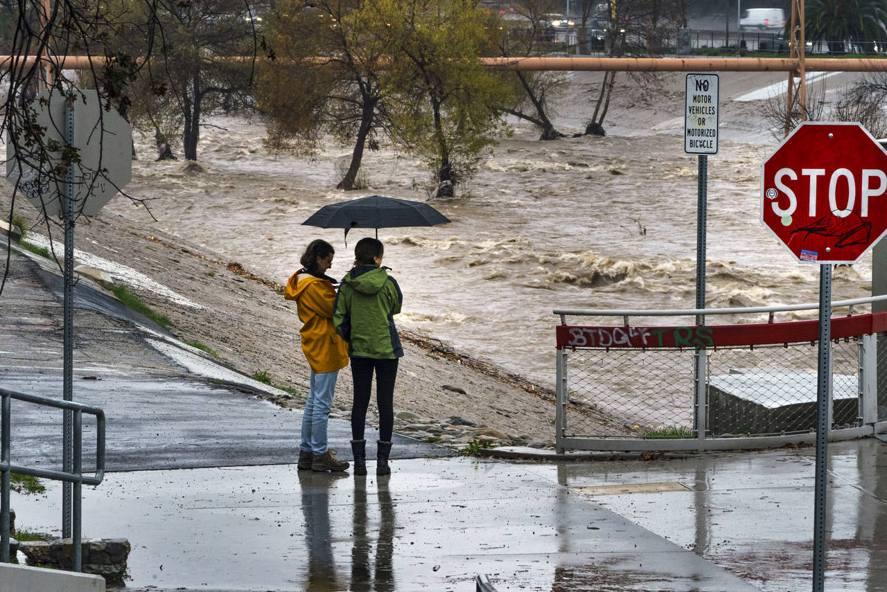 People watch the high volume of storm rain water flowing downstream at the Los Angeles River in Los...