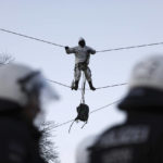 
              Police officers stay next to an activst who stands on a taut wire rope at the village Luetzerath near Erkelenz, Germany, Friday, Jan. 13, 2023. Police have entered the condemned village in to evict the climate activists holed up at the site in an effort to prevent its demolition, to make way for the expansion of a coal mine. (Rolf Vennenbernd/dpa via AP)
            